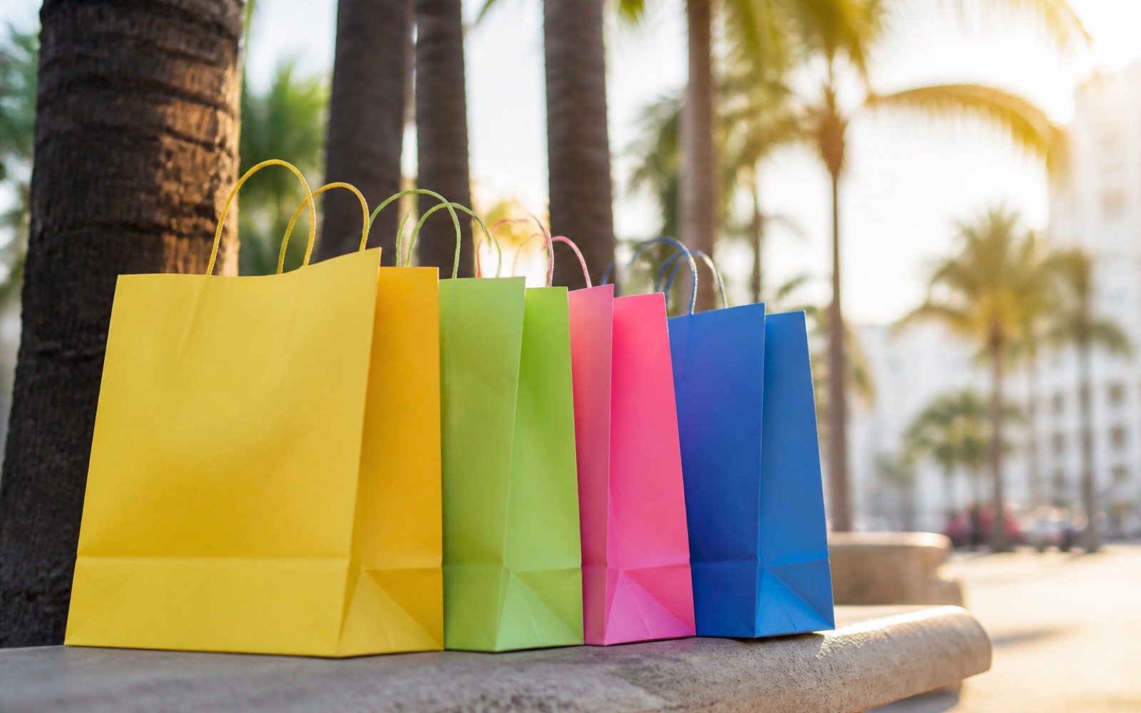 Bolsas de compras de colores sobre una banca, con palmeras al fondo